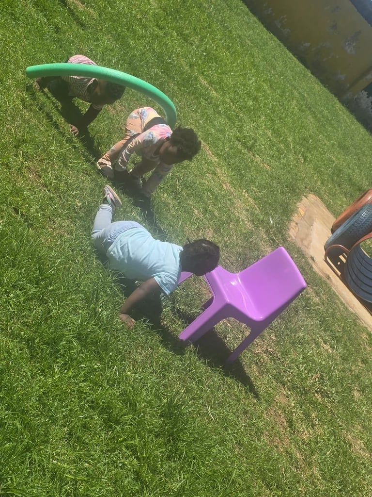 Aerial view of a person lying on grass playing with a green hula hoop and a pink toy chair nearby
