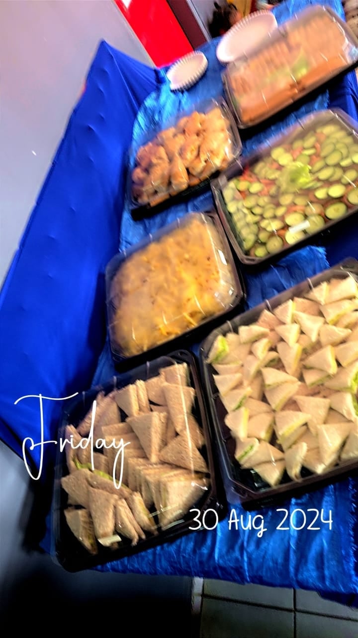 Multiple black containers filled with various snacks arranged on a blue surface with red utensils on top, dated 30 Aug 2024