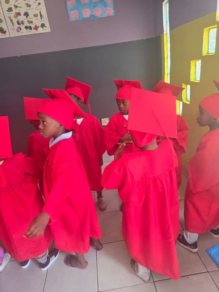 Group of young children wearing bright red graduation robes and caps in a classroom
