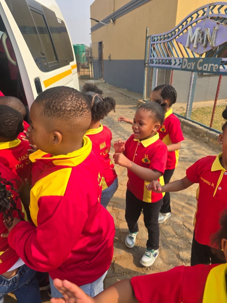 Group of children in red and yellow sports uniforms standing together outdoors near a school bus and gate