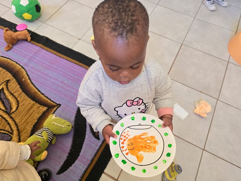Toddler in white shirt looking down at colorful plate with food on purple play mat indoors