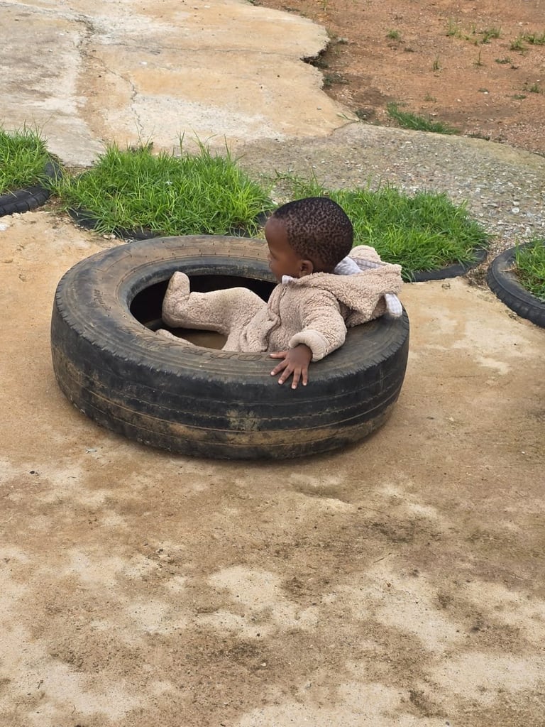 Young child crawling inside a large discarded tire on sandy ground outdoors