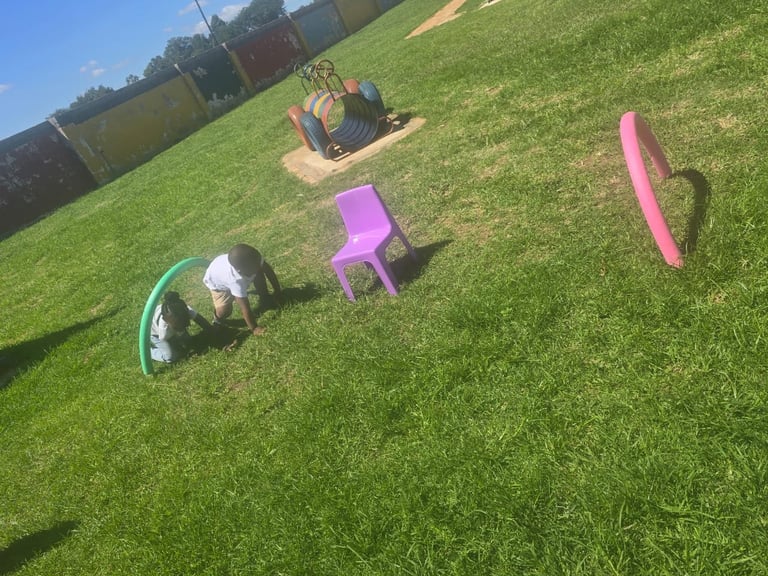 Outdoor garden scene with colorful items scattered on green grass including childrens toys and a purple chair