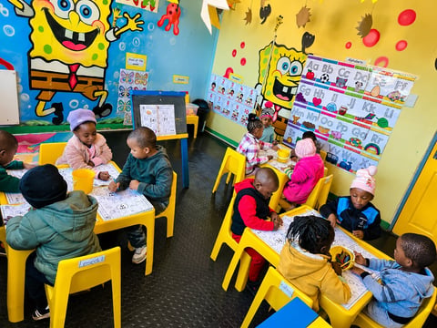 Children sit at yellow tables in a SpongeBob-themed classroom, engaging in activities and crafts.
