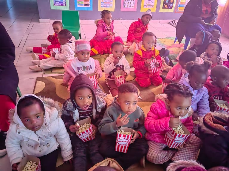 Group of young children sitting on floor holding popcorn containers at what appears to be a movie theater event or party