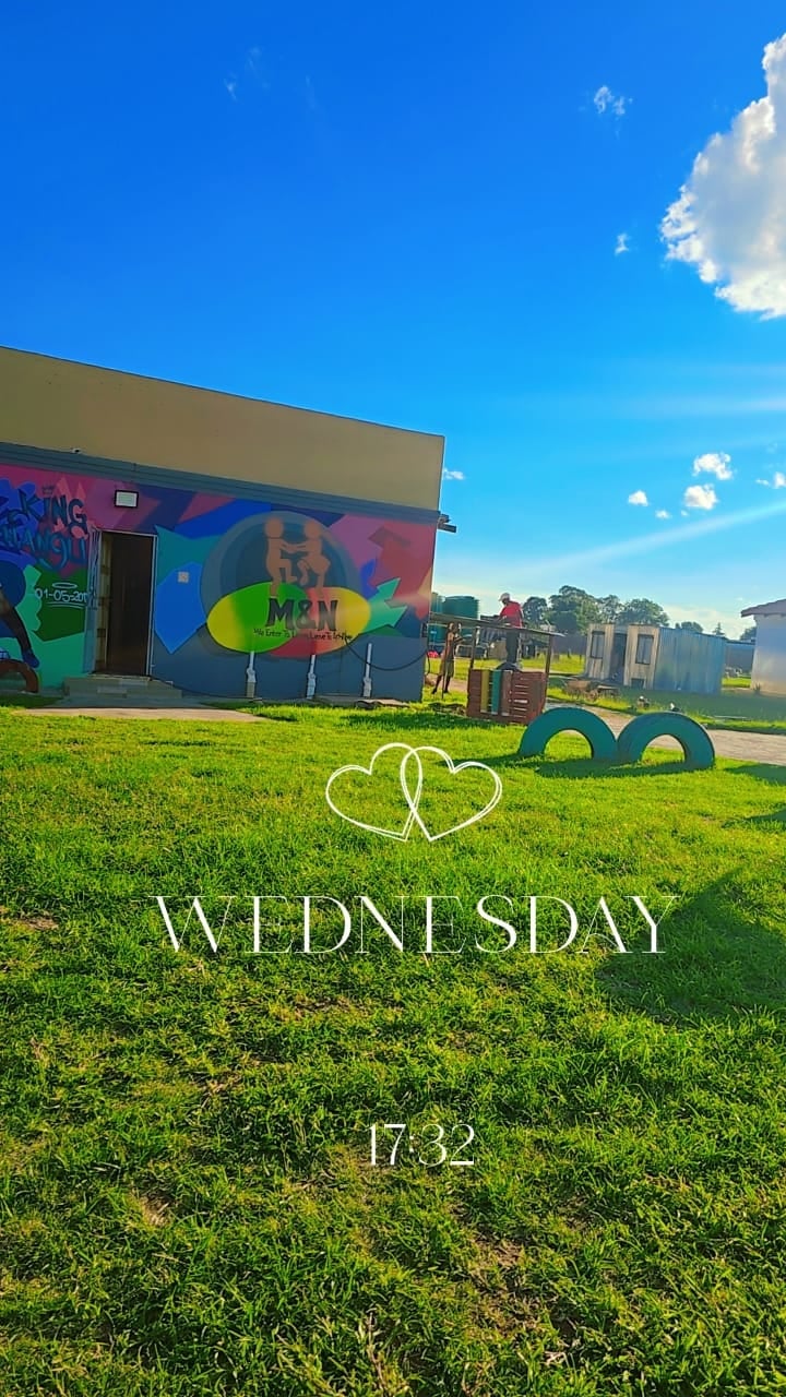 Colorful outdoor mural on building with green field, blue sky, and white text reading Wednesday 17:32 with heart icons overlay