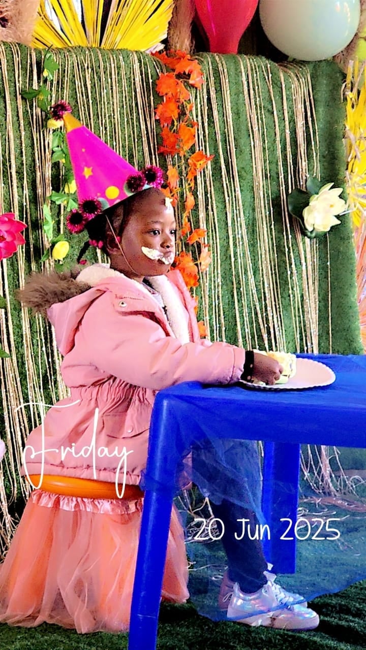 Child wearing pink jacket and colorful party hat sitting at blue table with festive decorations, dated June 20, 2025