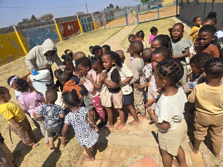 Group of African children gathered in a circle at a community playground with colorful equipment and fencing in the background
