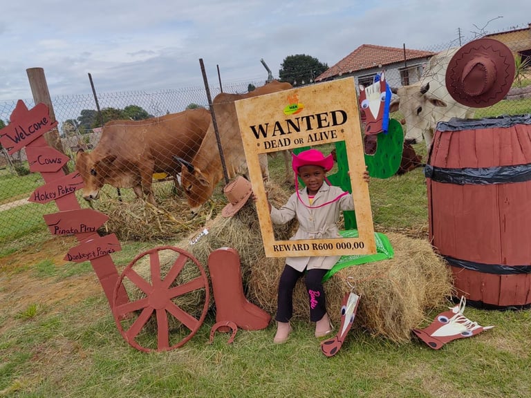 Person posing with wanted poster at Western-themed farm attraction with cow, wagon wheel, and rustic props