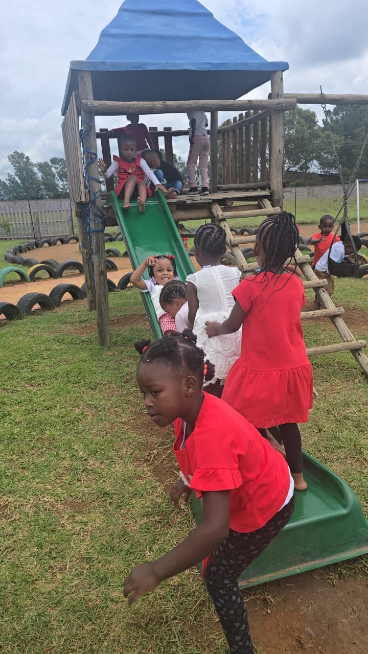 Children playing on a wooden playground structure with a green slide and blue roof in an outdoor school setting