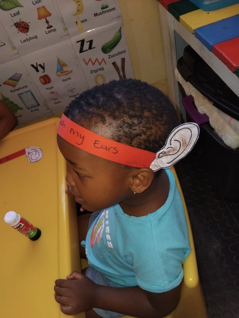 Child wearing orange headband with ear cutout and blue shirt in classroom setting with educational posters and storage bins