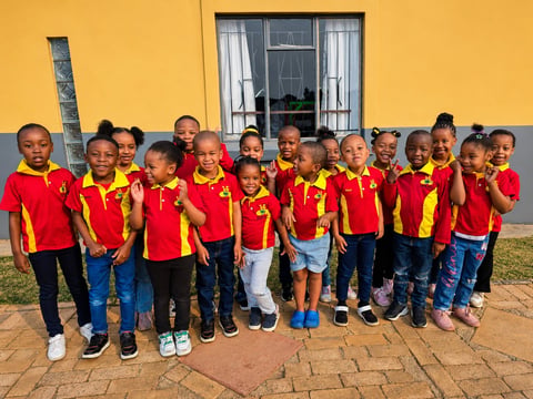 Group of young children in red and yellow uniforms standing together in front of a yellow building