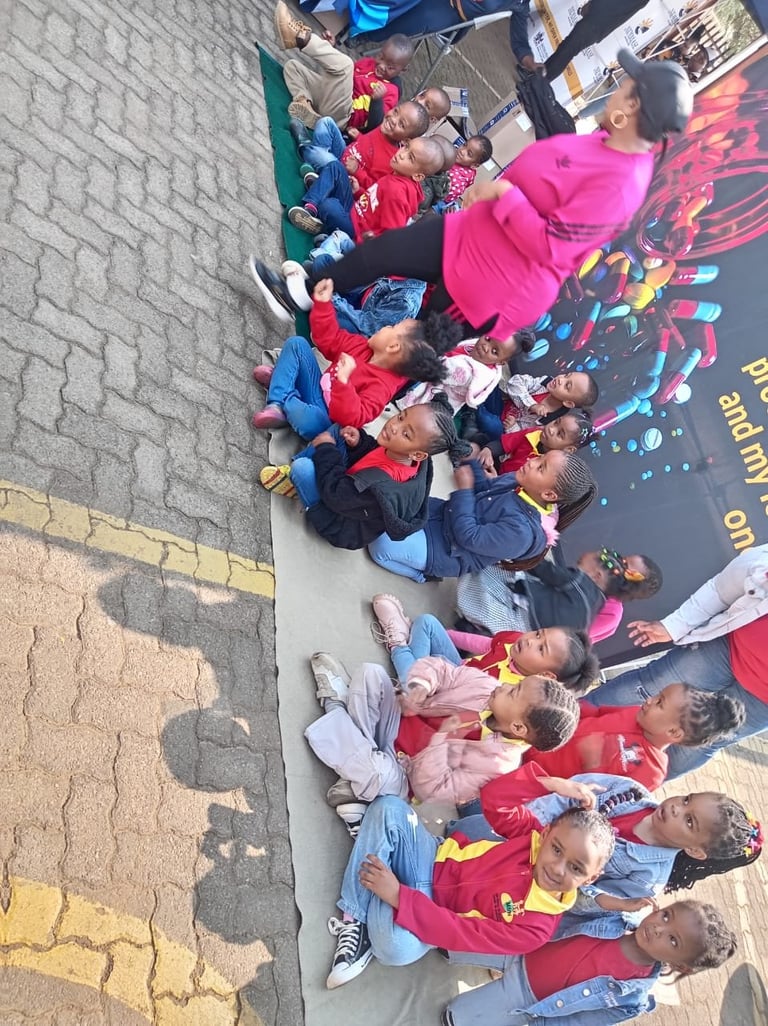 Large group of children in colorful clothing sitting together outdoors on a paved surface, viewed from above