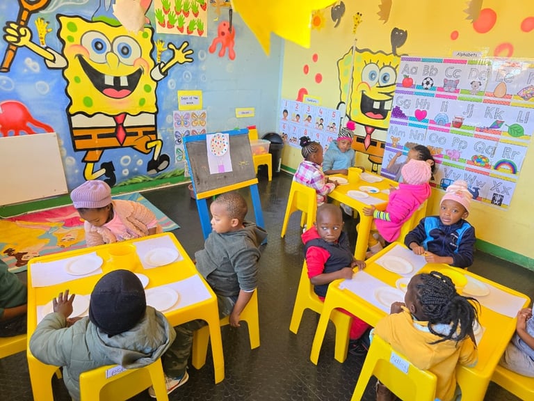Classroom of young children sitting at yellow tables with SpongeBob SquarePants decorations on walls and shelves with supplies