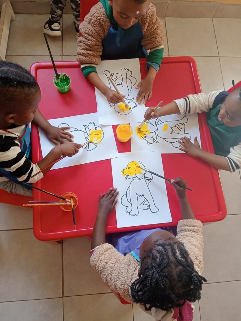 Children painting sun drawings together at a red table during an art activity