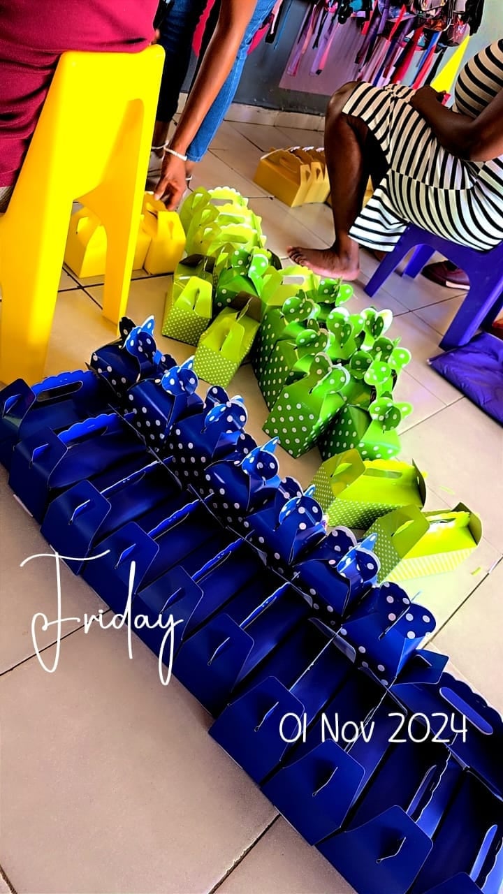 Colorful plastic gift bags in blue, green, and yellow arranged on floor with people standing nearby, dated Friday 01 Nov 2024