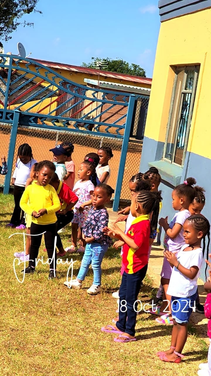 Group of children gathered outdoors in a yard next to a yellow house with a blue metal structure, dated October 18, 2024