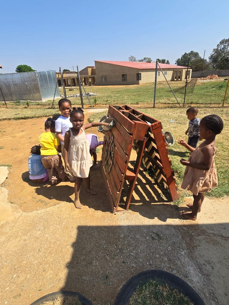 Group of children standing around a wooden ox cart in a rural African village compound on dusty ground