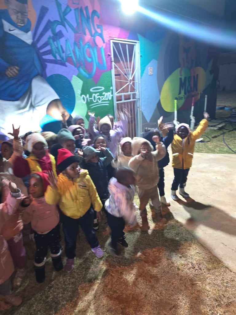 Group of children with hands raised dancing in front of colorful graffiti wall with neon pink and blue lighting