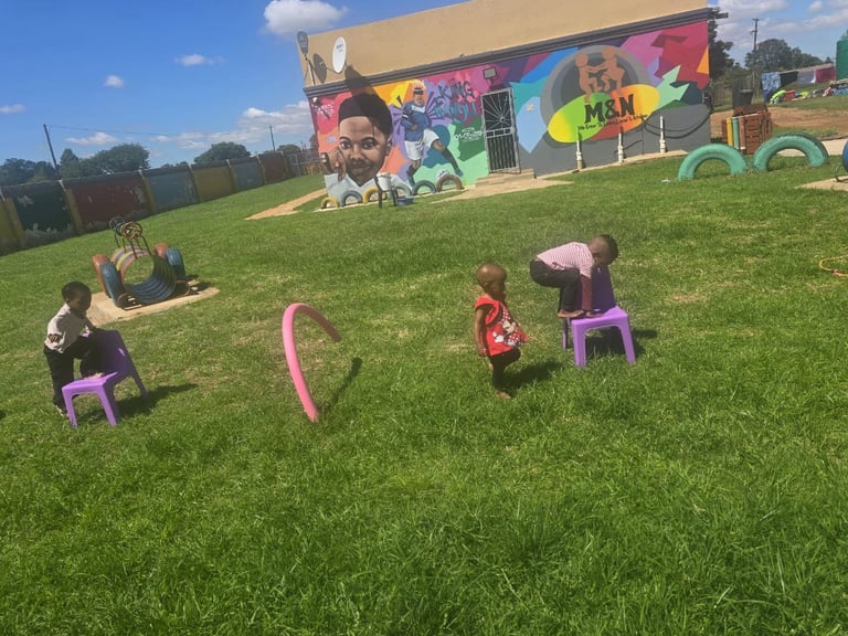 Children playing with pink playground equipment on a grass field with a colorful mural building in the background