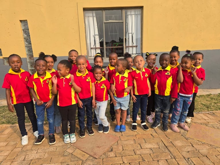 Group of children wearing red and yellow uniforms standing together in front of a yellow building