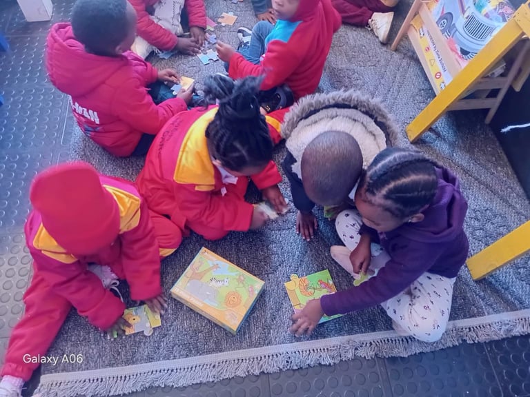 Group of young children in red jackets sitting in a circle on carpet, engaged in learning activity with picture books