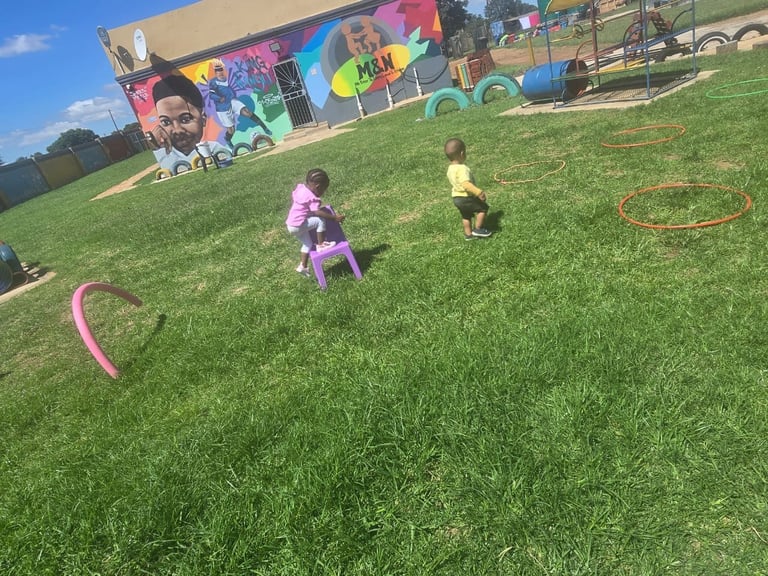 Children playing outdoors on a grass field with colorful hula hoops and a large mural-painted building in the background