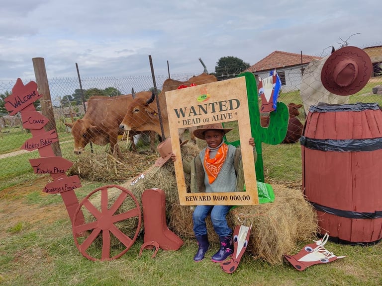 Person posing behind humorous Wanted poster prop with cow, hay bales, and rustic farm decorations in rural setting