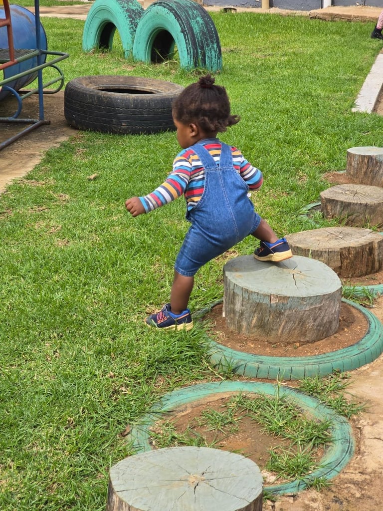 Child playing on outdoor obstacle course with wooden stumps and recycled tires on grass
