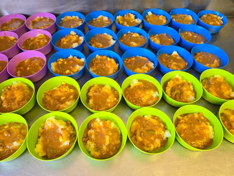 Multiple rows of colorful bowls containing yellow curry or stew arranged on a surface in pink, blue, and green containers