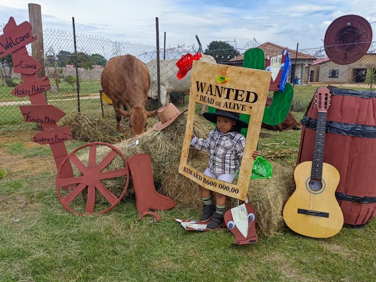 Child posing in Western-themed Wanted poster cutout with cow, guitar, and rustic props at farm attraction