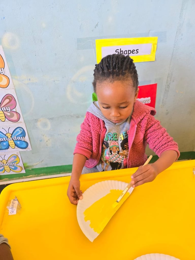 Young child in pink cardigan engaged in hands-on shape learning activity at a bright yellow classroom table