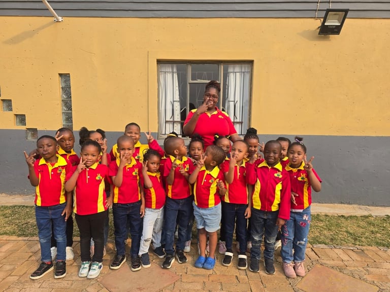 Group of children in red and yellow uniforms standing with an adult in front of a yellow building